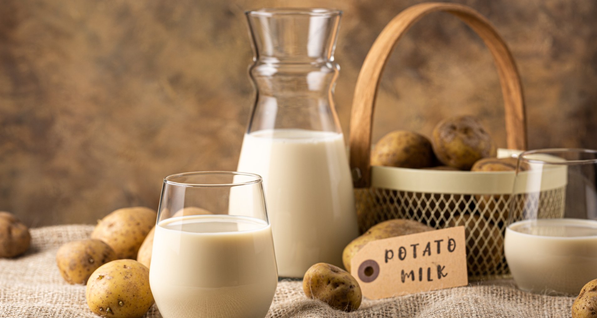 Стакан молока и бутылка на фоне корзины на скатерти рядом с картофелем