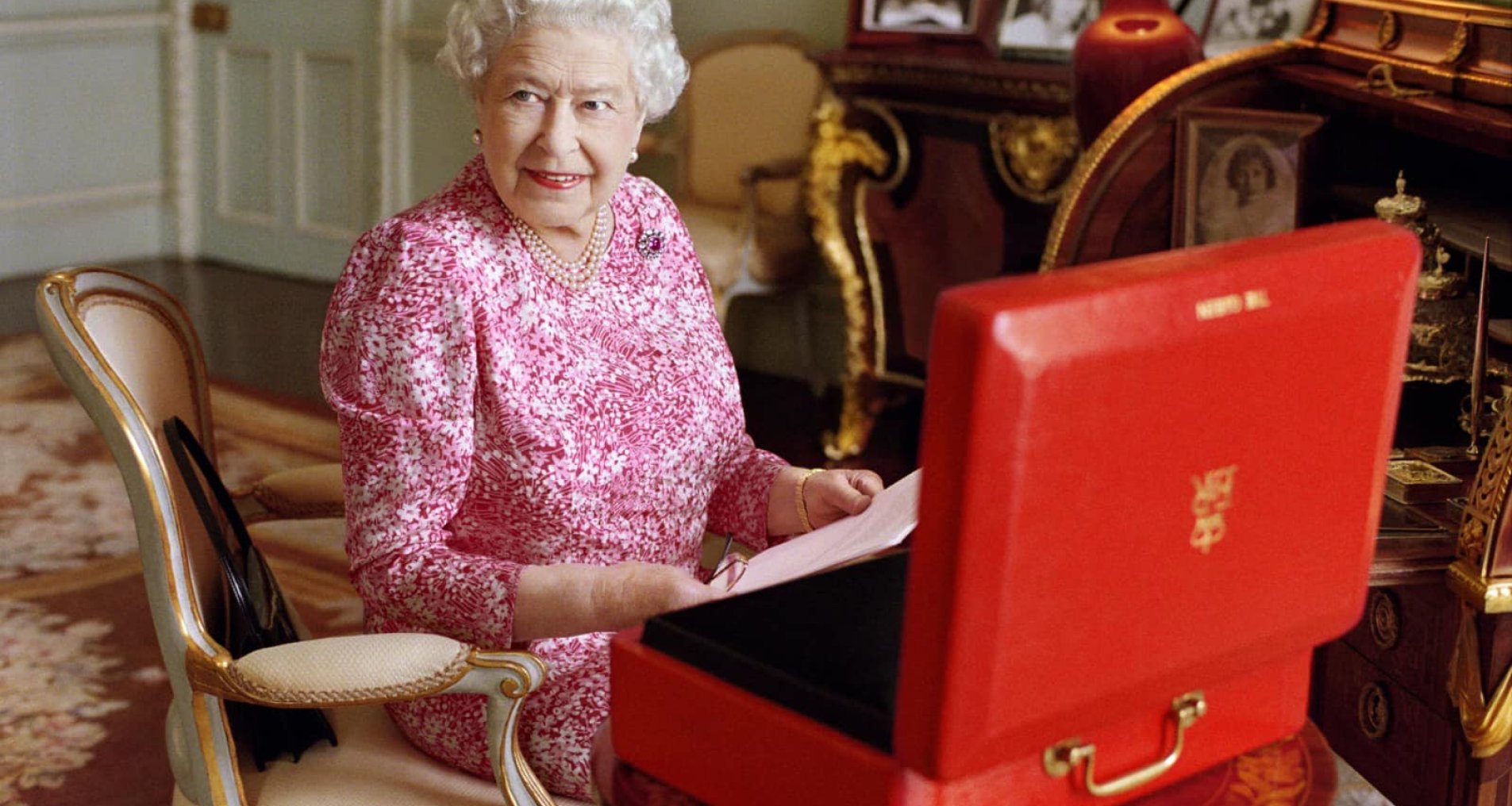 Королева Єлизавета ІІ сидить у кріслі перед червоним кейсом