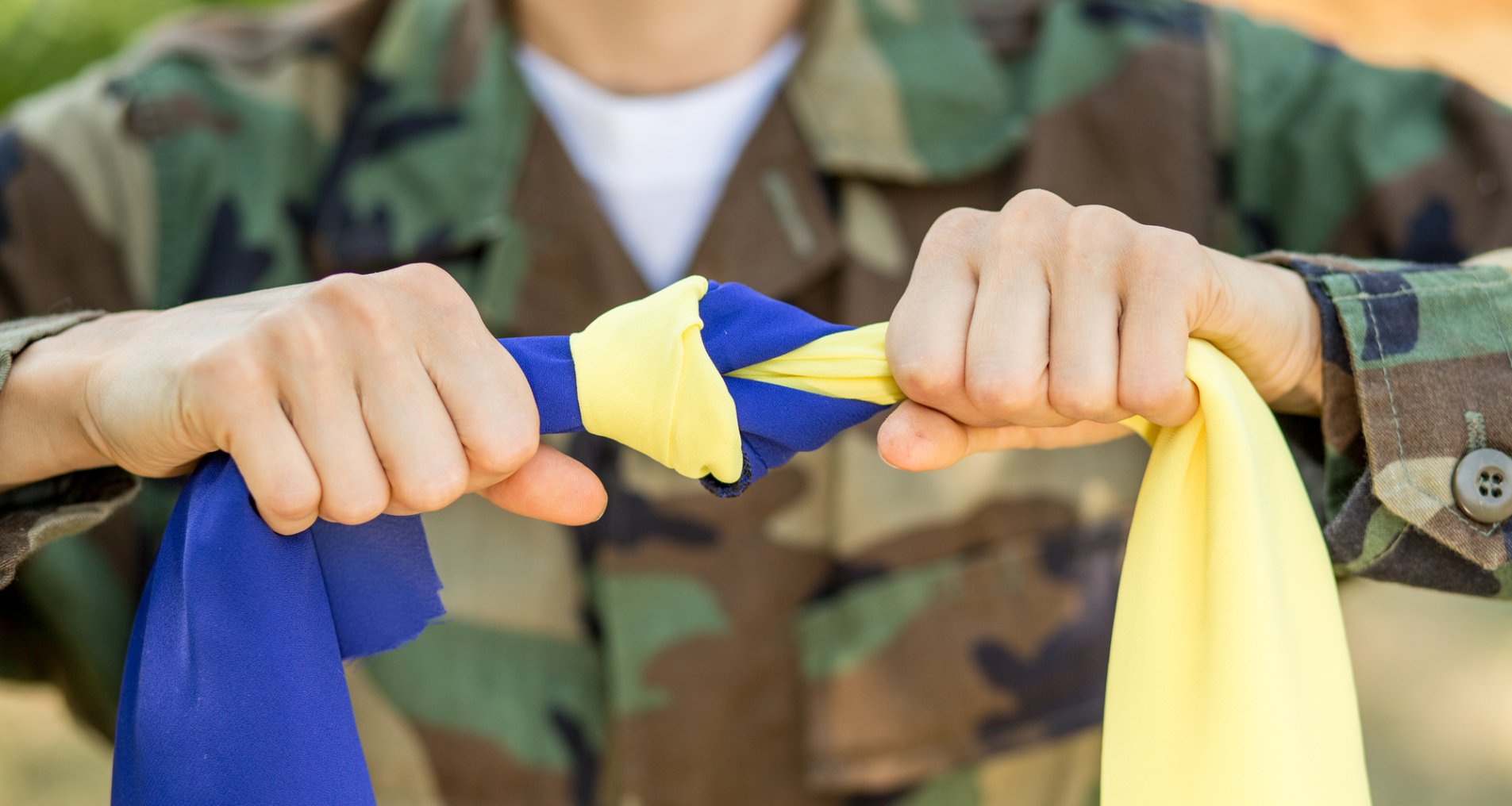 Молодой человек в военной форме держит завязанный флаг Украины