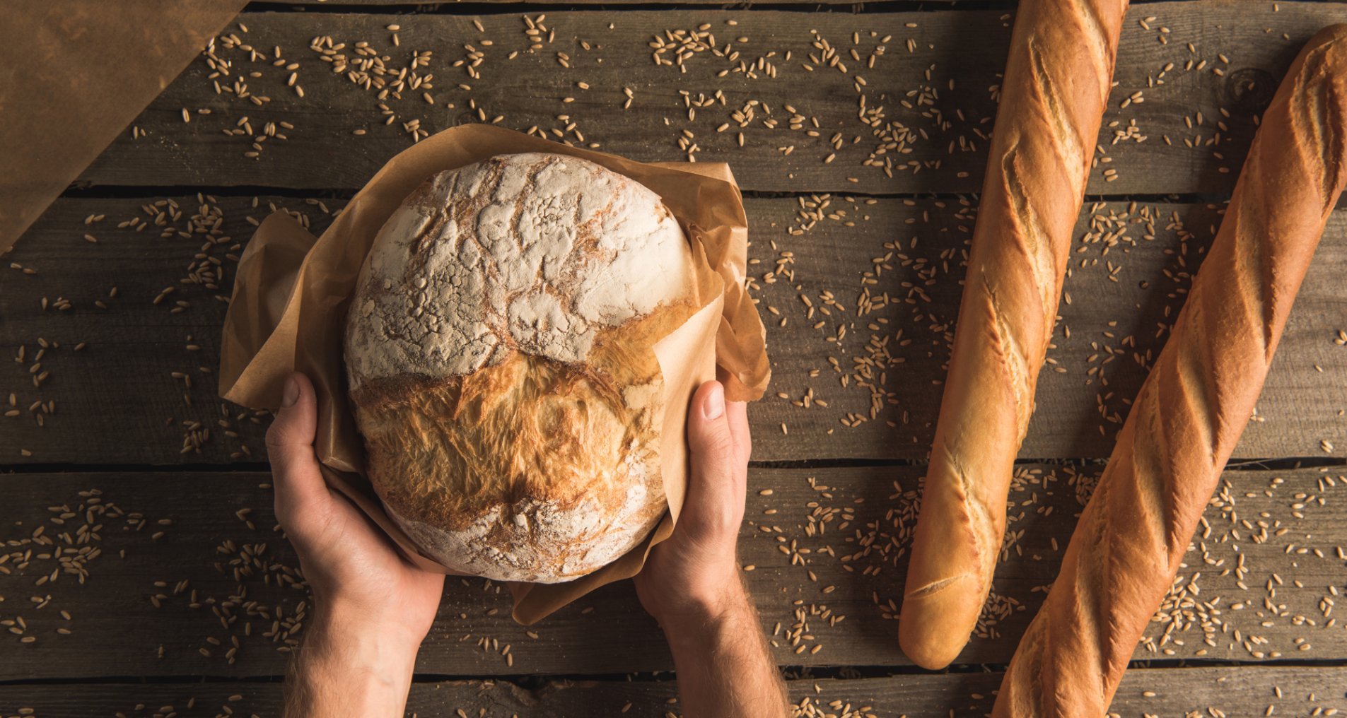 Хлеб и два багета с руками на фоне деревянного стола