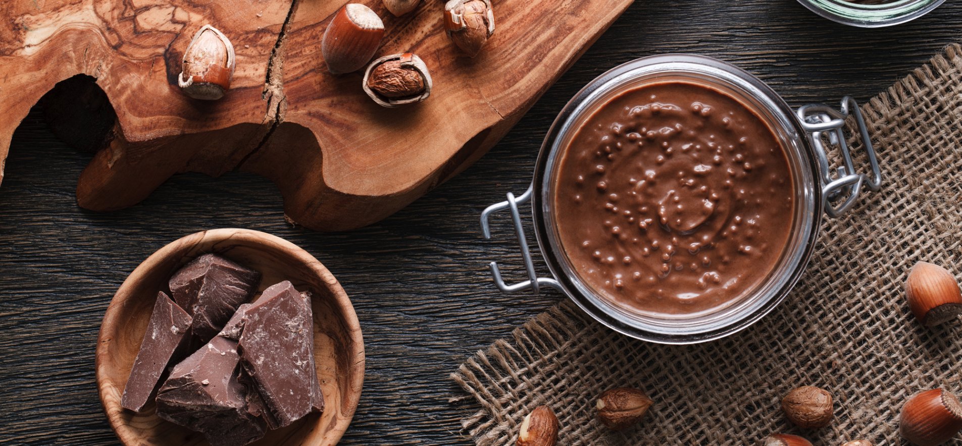 Шоколадний соус у банці поруч із шоколадом та горіхами навколо